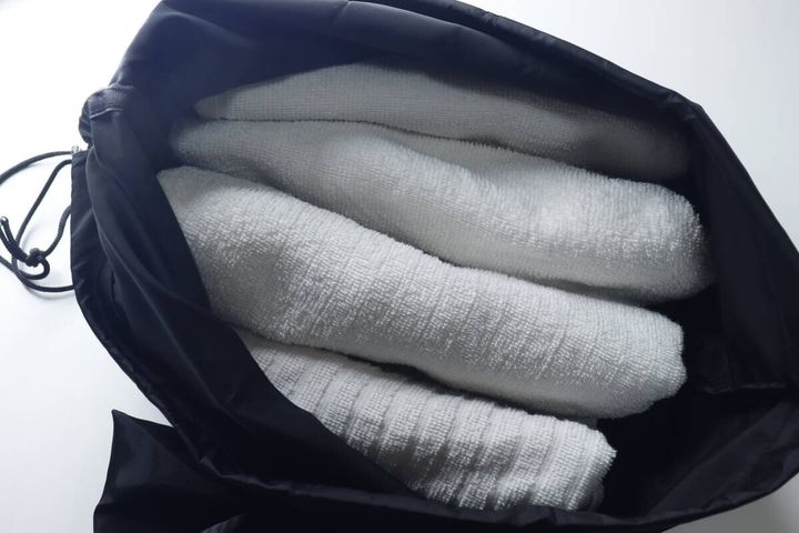 黒いナップサックの中に白いバスタオルが4枚入っている
