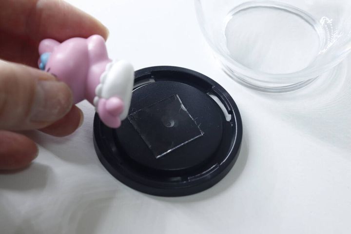 手がピンク色のうさぎのフィギュアを、両面テープが貼られた黒い台座に置こうとしている