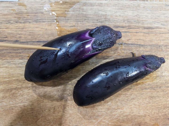まな板に置かれた2本のなすに竹串で穴を開けている様子
