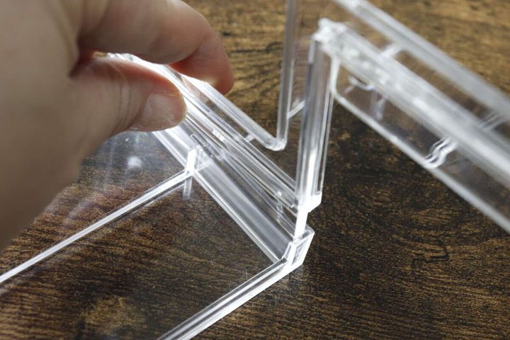透明なディスプレイステージのパーツを指で差し込んで組み立てている手元