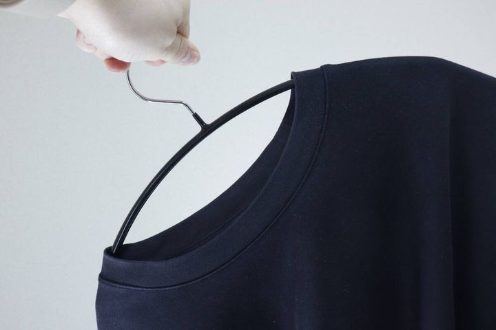 黒いTシャツの首元にハンガーを差し込んでいる手元