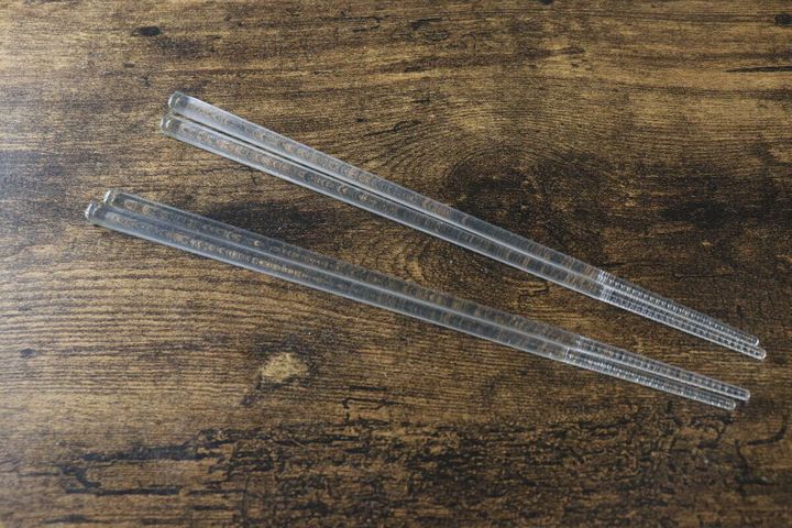 木目のテーブルに斜めに置かれた透明なクリア箸2膳