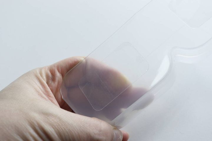 半透明のメガネ収納本体の裏側にある粘着テープ部分を指で示している
