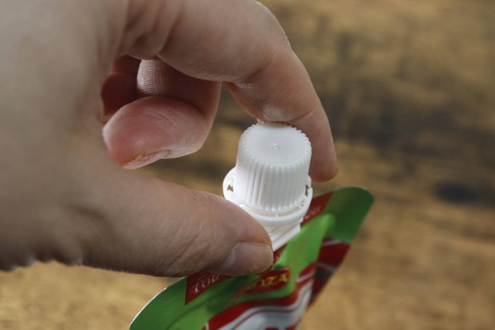指でパウチの白いキャップを回して開けようとしている手元のクローズアップ
