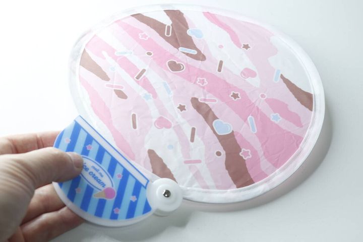 広げたアイスクリーム柄のうちわと、持ち手となるケースを握る手