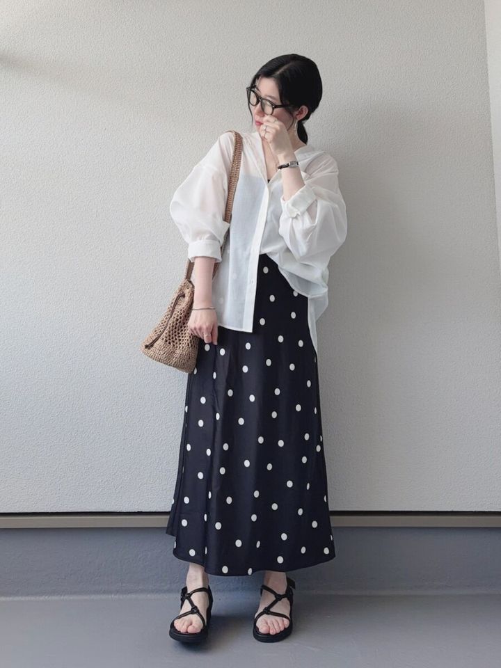 黒ドット柄スカートに白シアーシャツを着て眼鏡をかけた女性