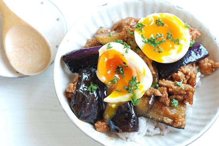 白いご飯の上に盛り付けられた、なすとひき肉の味噌ケチャ炒めと半熟ゆで卵。横に木製スプーン