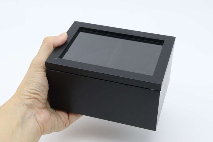 黒い腕時計用収納BOXを片手で持ち上げている