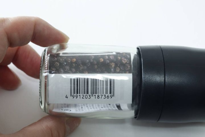 手で持ったペッパーミルの側面に貼られたバーコードと商品情報