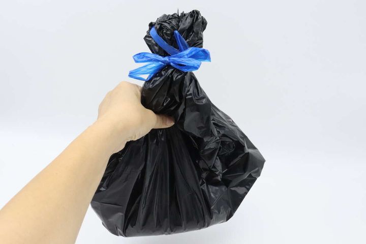 青い紐でしっかり縛られた黒いビニール袋を手に持つ