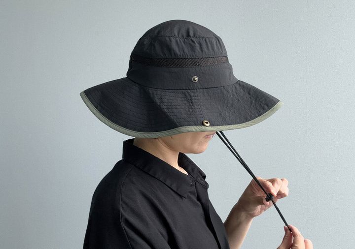 黒いサファリハットを被った女性が顎紐を調整している横顔。