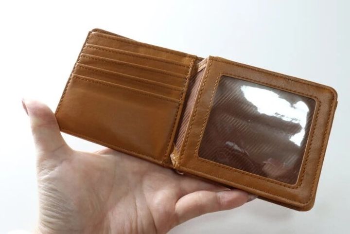 女性の手が茶色の二つ折り財布を開き、カード入れとクリア窓が見える
