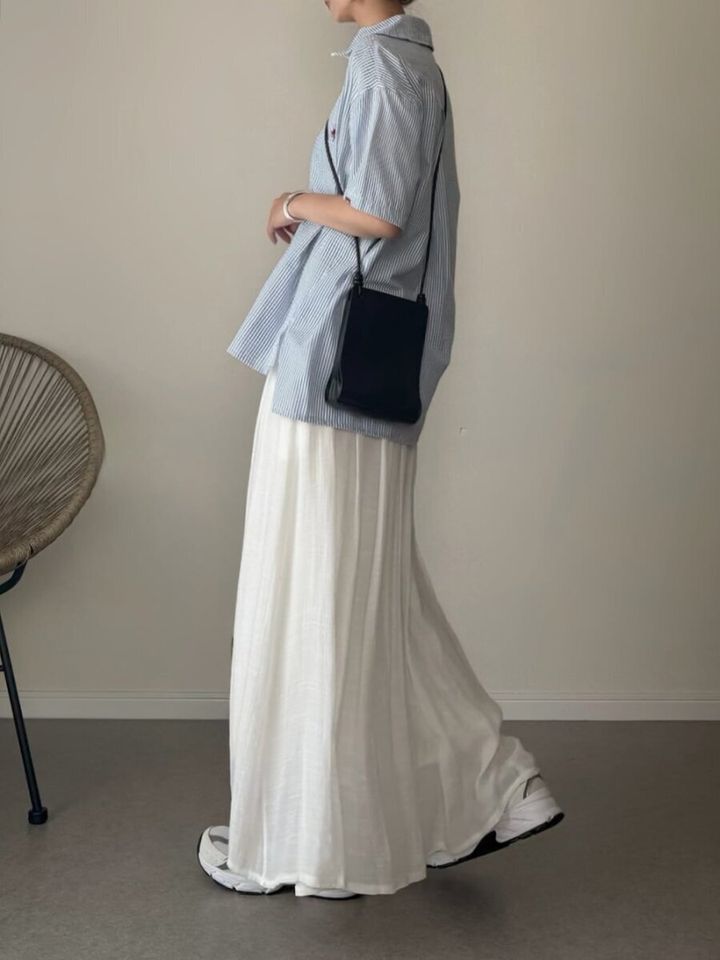 ブルーストライプシャツと白いロングスカートを着用し、横向きに立つ女性