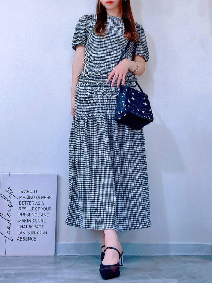チェック柄セットアップを着た女性が黒いバッグを持ち立つ