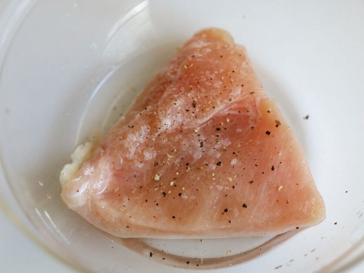透明なボウルに入った鶏むね肉に、塩こしょうと酒をもみ込んでいる様子