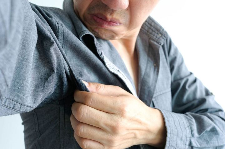 腕を上げ、腋に顔を近づけてにおいを確認している男性