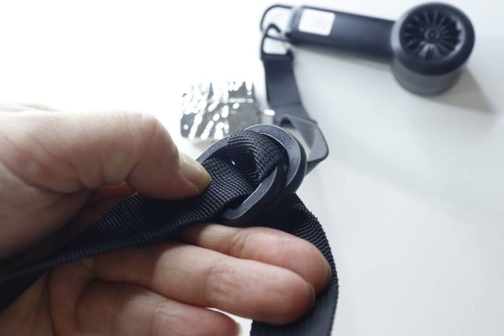 手が黒い平紐ロングストラップの長さ調節Dカン部分を触っているクローズアップ