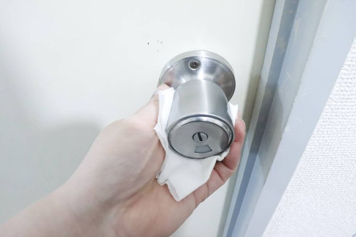 白いシートでステンレス製のドアノブを拭いている手元
