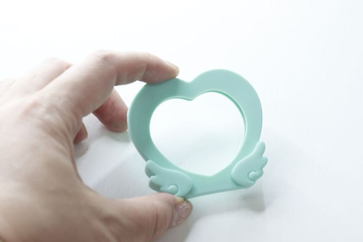緑色のハート型シリコン缶バッジスタンドを指で持つ手元