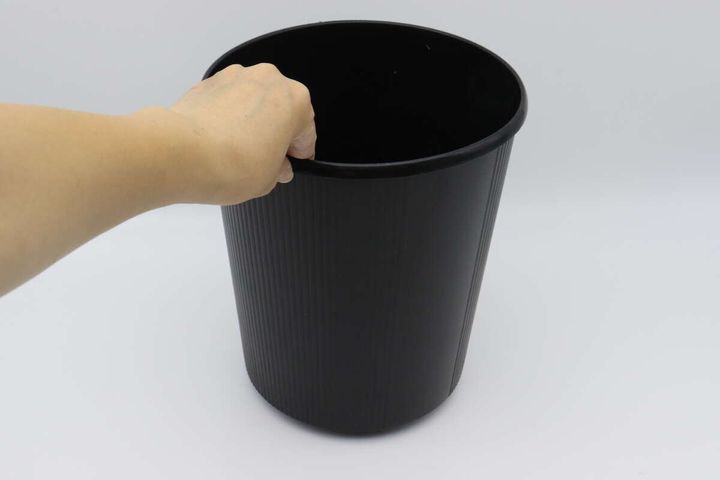 ボールキャスターを取り付けた黒いゴミ箱の縁を持ち上げている手