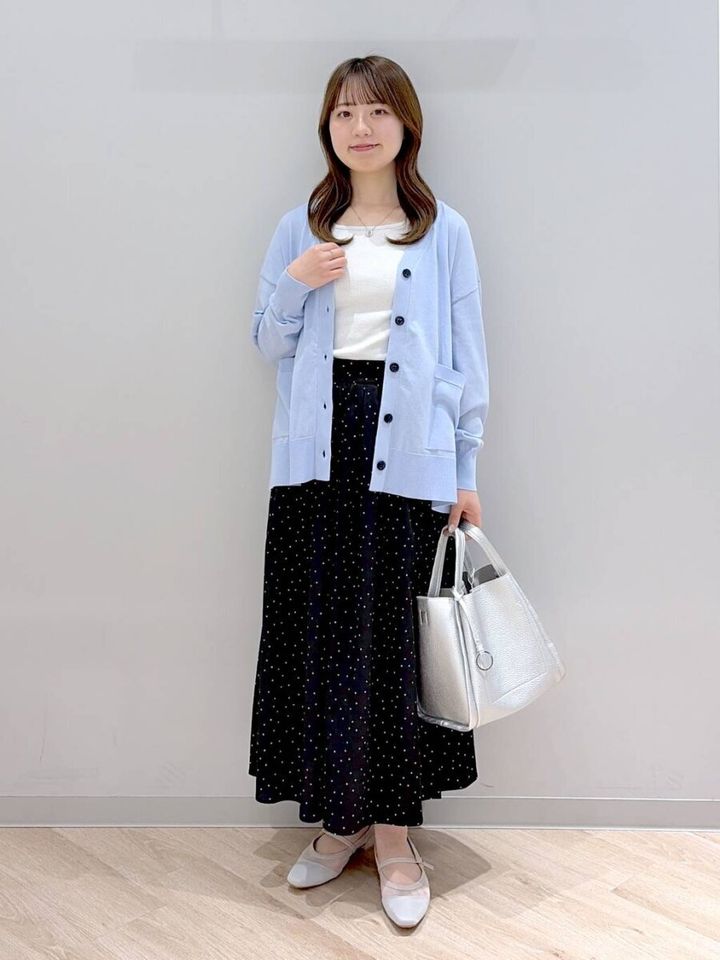 水色の長袖カーディガンとドット柄ロングスカートの女性が立っている