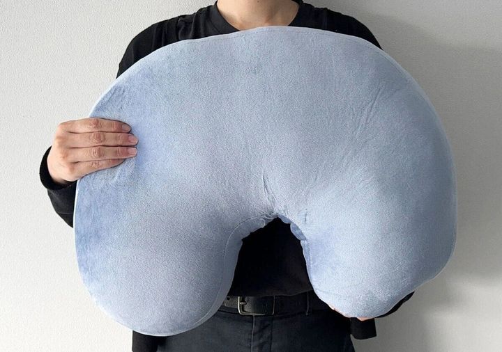 青いU字型クッションを両手で抱えている男性
