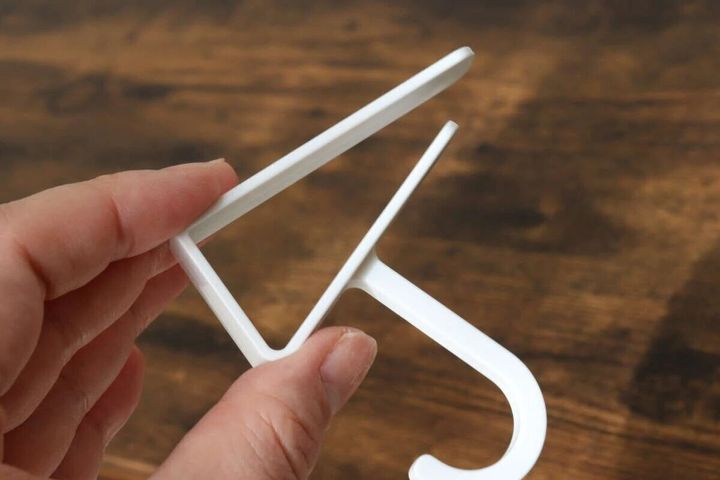 白い吊り戸棚用フックを指でつまんで見せている
