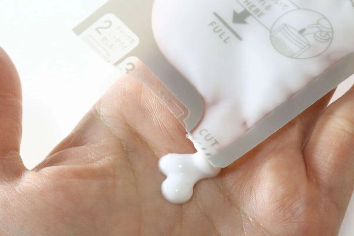 詰め替えパウチから乳白色の液体を手のひらに出している