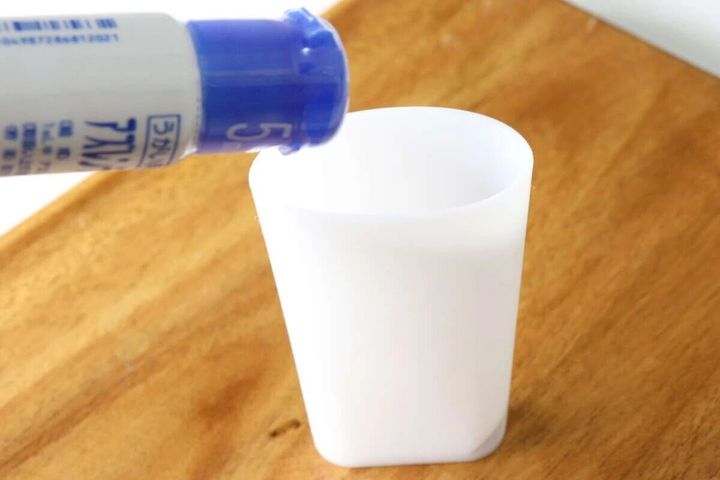 白いスリムコップに青いボトルから液体を注ぎ入れている