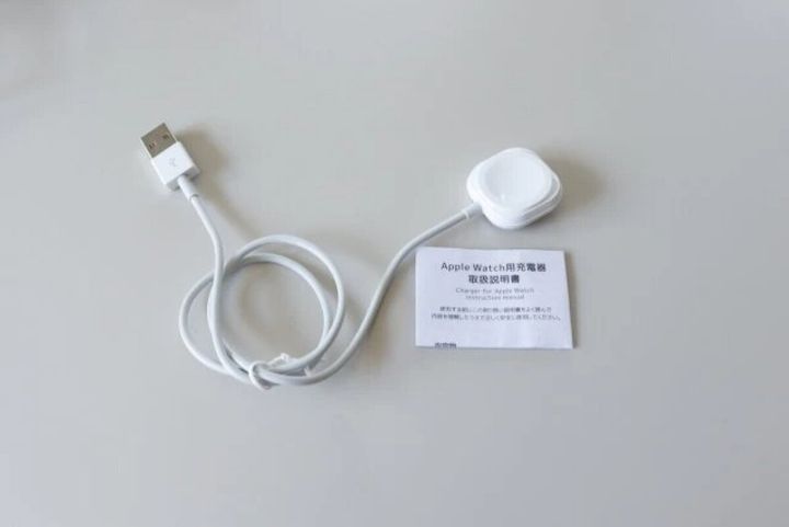 白いスマートウォッチ充電器とUSBケーブル、取扱説明書が写っている