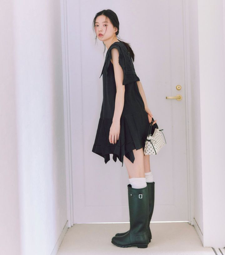 ジェニーの着こなしをお手本にした、片山友希の大人ガーリーなモノトーンコーデ。イレギュラーヘムが今っぽい黒のミニワンピースに、白のルーズソックスと黒のロングレインブーツを合わせ、ドット柄のミニバッグを持った最旬の脚見せスタイル。