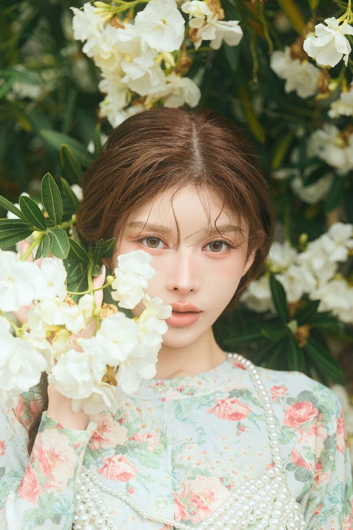 白い花を背景に、花柄の服を着た齊藤早紀さんがカメラを見つめている