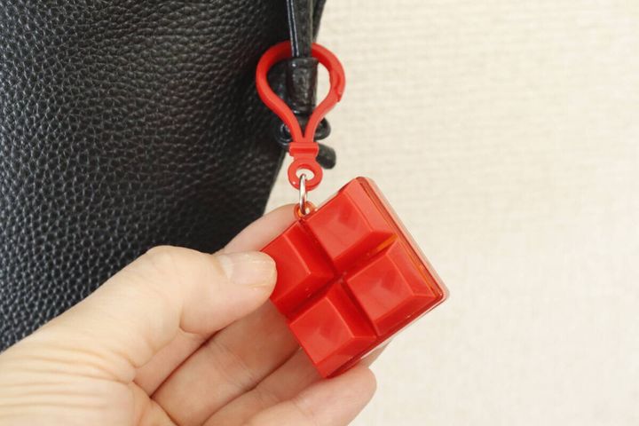 黒いバッグに付けられた赤いキーホルダーを指でつまんで見ている