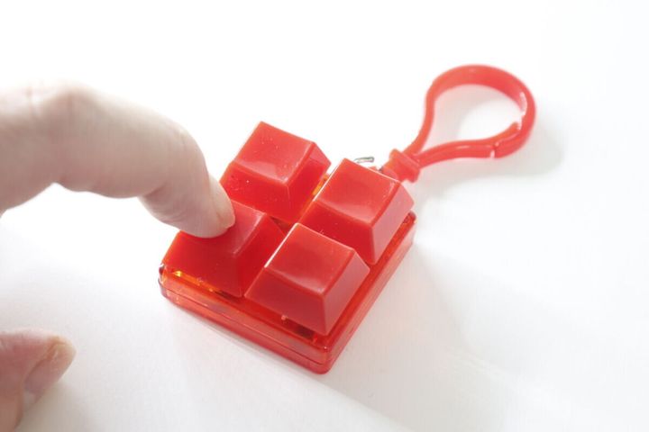 指で赤いカラーブロックキーホルダーのボタンを押し込んでいる様子