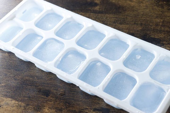 水が凍って氷になった状態のアイストレーが木目のテーブルに置かれている