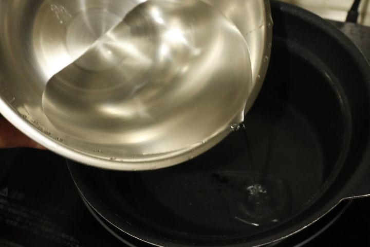 ステンレスボウルに入った水を黒い鍋に注ぎ入れている手元
