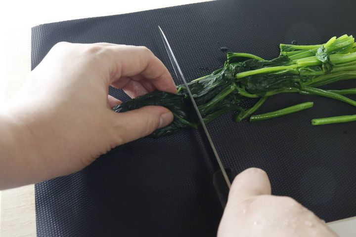 黒いまな板シートが敷かれたまな板の上で、手がほうれん草を包丁で切っている