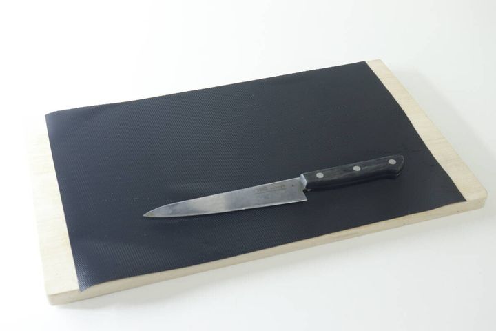 木製のまな板の上に黒いまな板シートが敷かれ、その上に包丁が置かれている