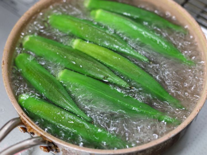 鍋で沸騰したお湯の中で茹でられているたくさんのオクラ