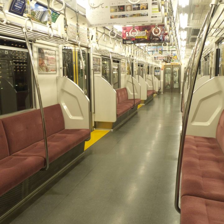 赤い座席とつり革が並ぶ、夜の空いた電車の車内