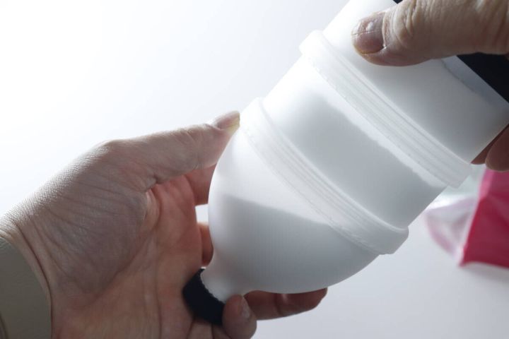 手が白いプロテイン容器を逆さに持ち、漏斗として使う準備をしている様子