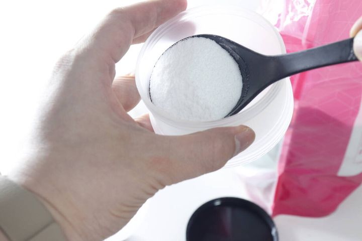 手が白い容器にスプーンで白い粉末プロテインを入れている様子