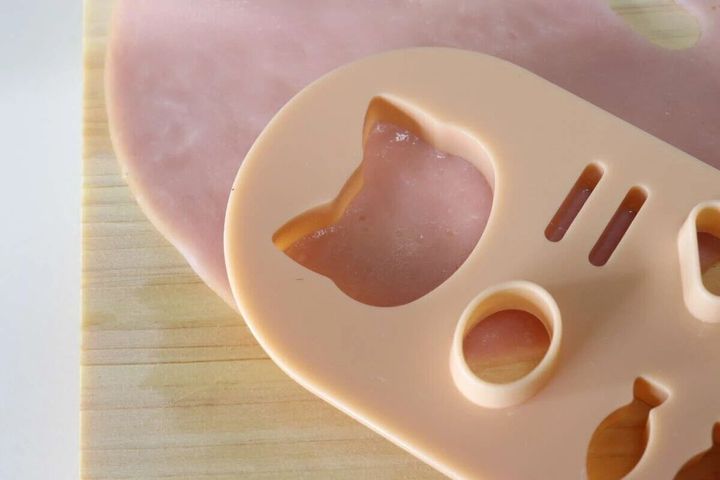 ハムの上にねこ型抜きプレートを置き型抜きしている