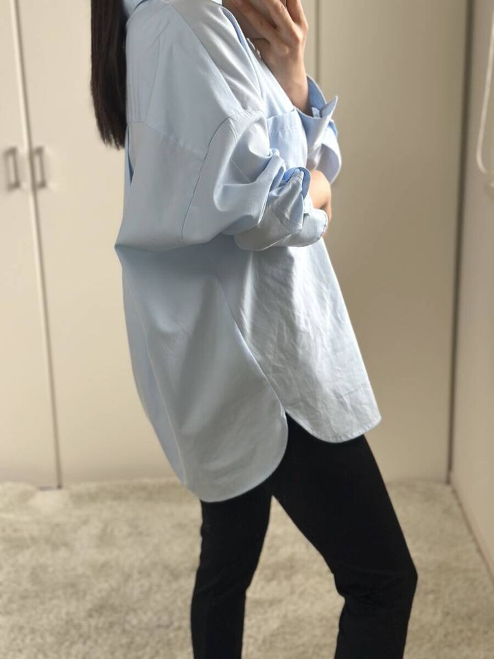 サックスシャツを羽織り黒パンツを履いた女性の横姿