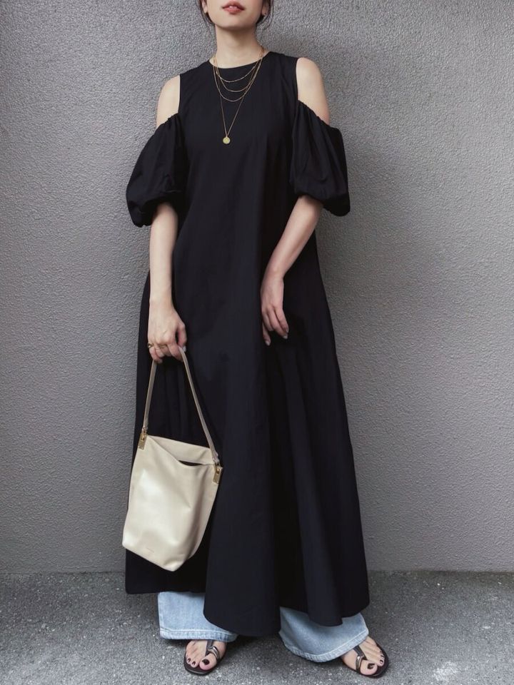 黒のオープンショルダーワンピースにデニムをレイヤードし、ベージュのバッグとサンダルを合わせた女性の全身