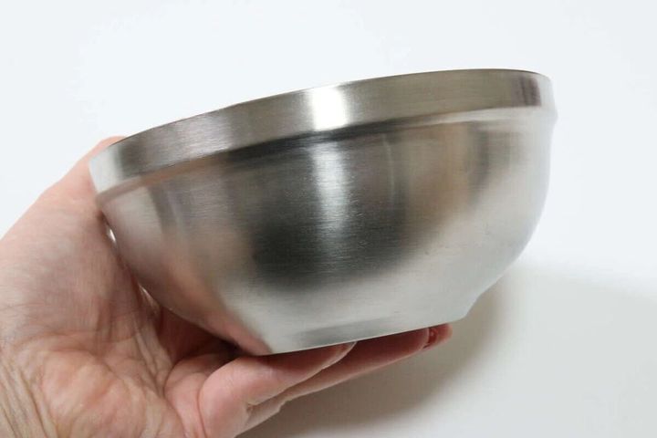 女性の手がシルバーの光沢があるステンレス製茶碗を持っている