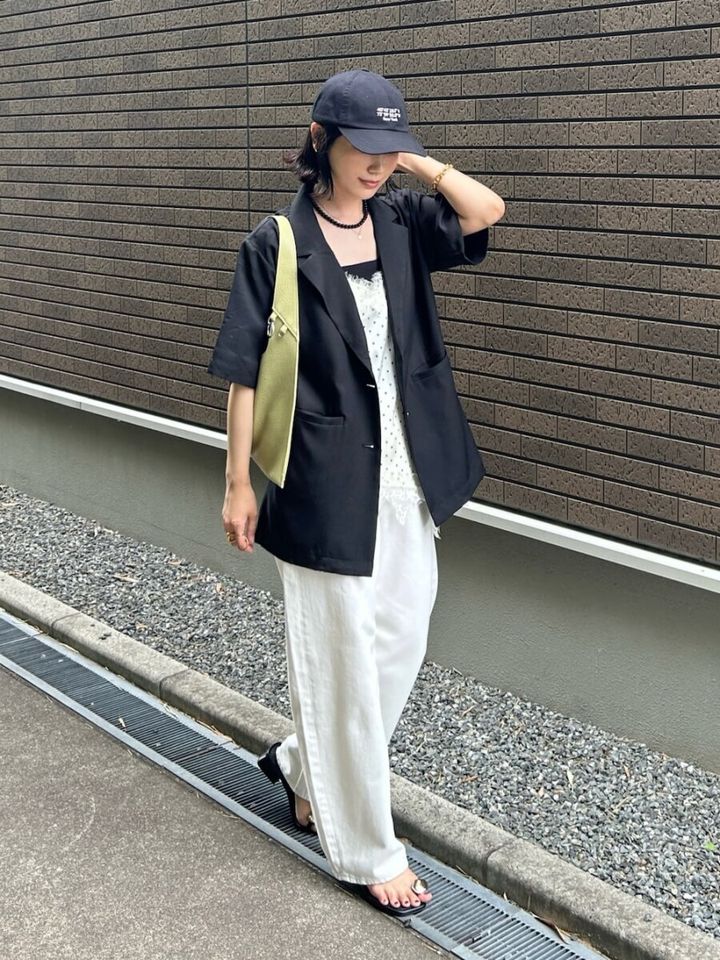 黒の半袖ジャケットと白ワイドパンツ、キャップを被った女性が歩いている。