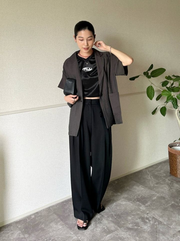 濃いグレーの半袖ジャケットと黒のロゴトップス、黒ワイドパンツを着た女性。