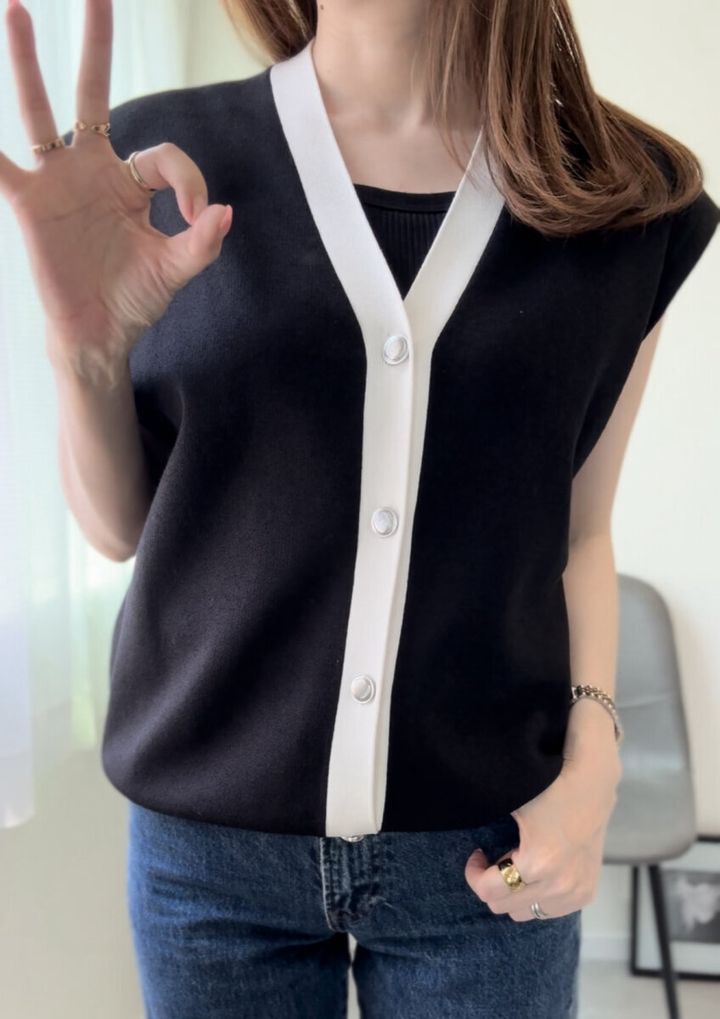 黒いブラキャミに白黒のVネックニットを重ね着した女性がOKサインをしている