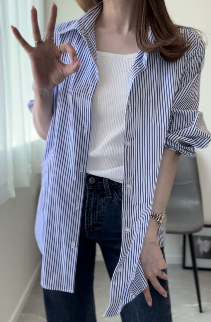 白いブラキャミにストライプシャツを羽織った女性がOKサインをしている